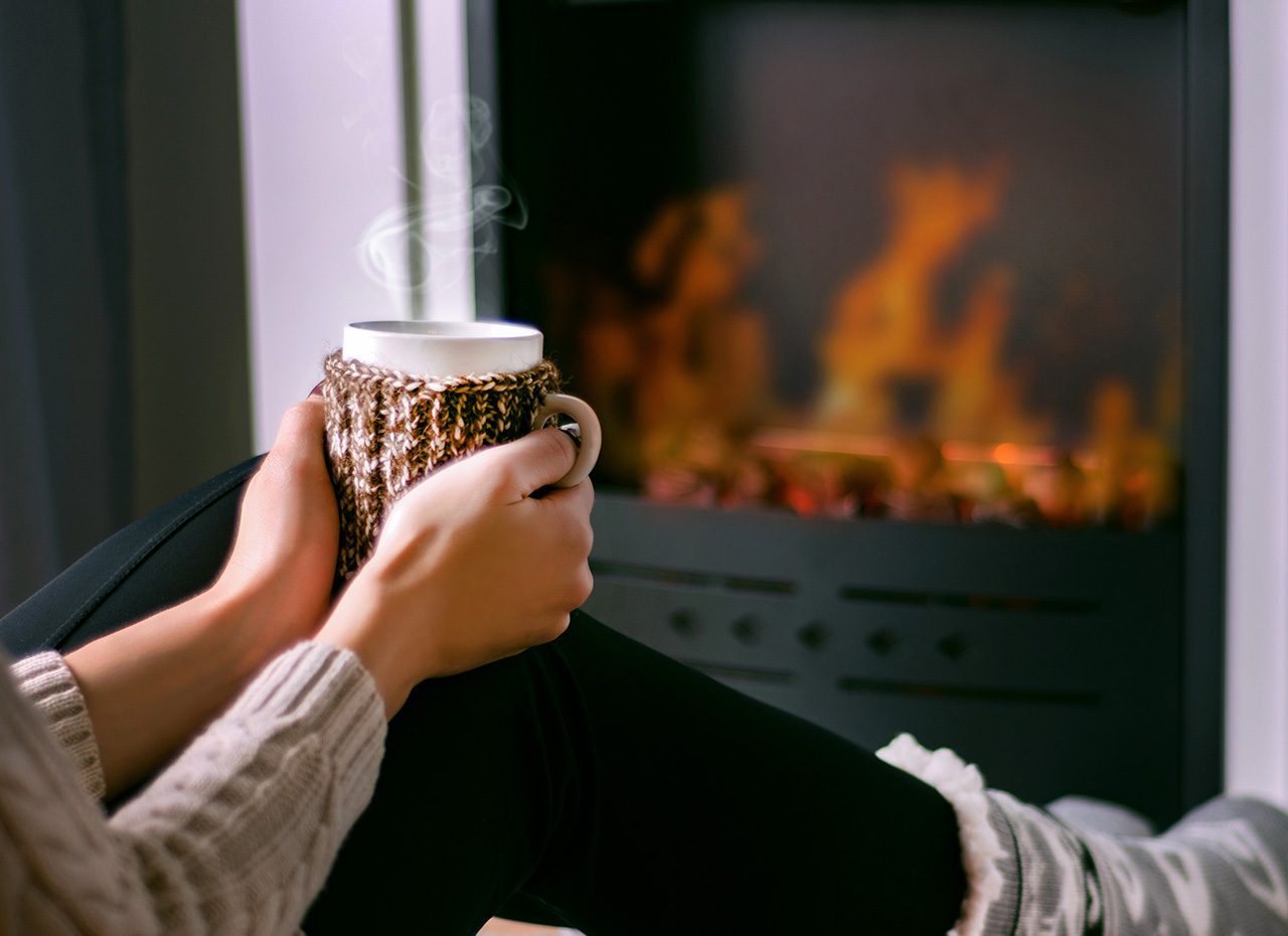 Hands holding a warm beverage with steam rising from it while sitting in front of a fire. winter storms