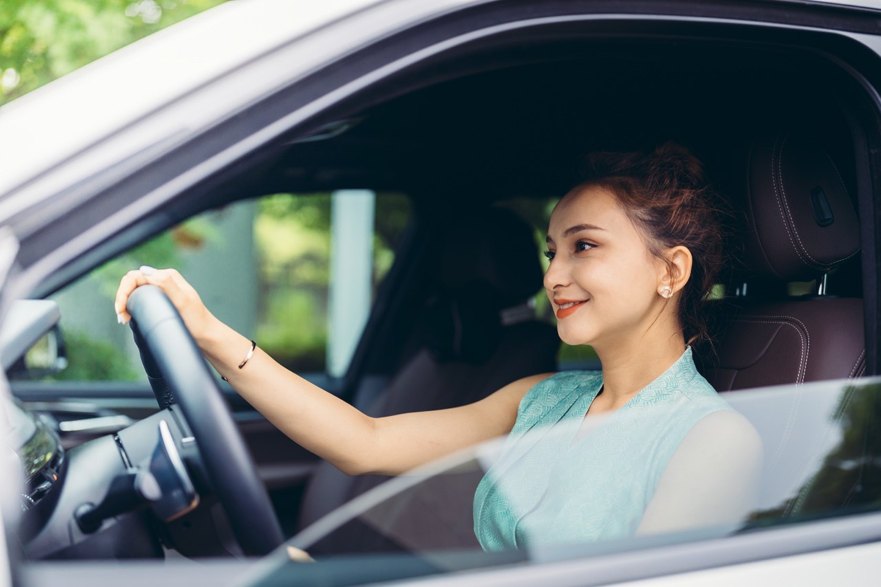 A view through the driver side window of a smiling woman driving a car. aggressive driving