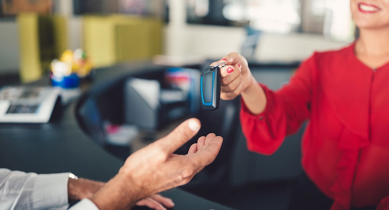 A woman hands over keys to an outstretched hand at a rental car counter. rental car insurance