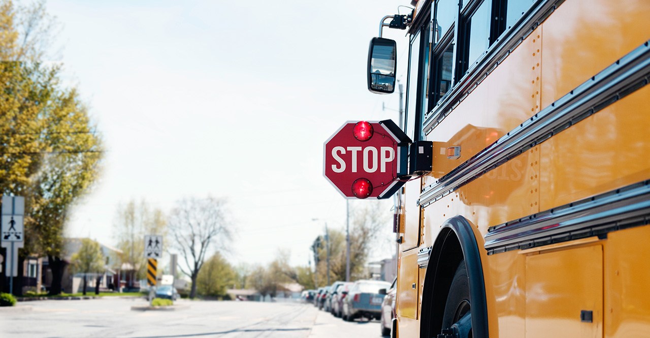 A flashing stop sign sticks out from a stopped school bus. back to school