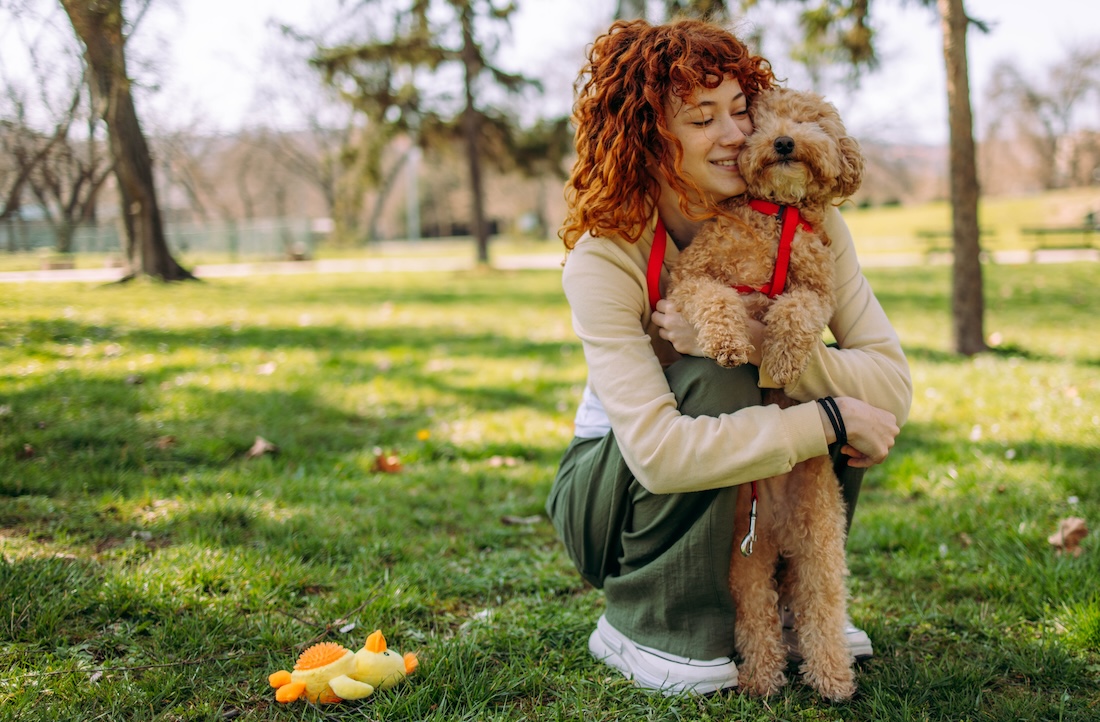 A woman embraces her golden doodle in the park