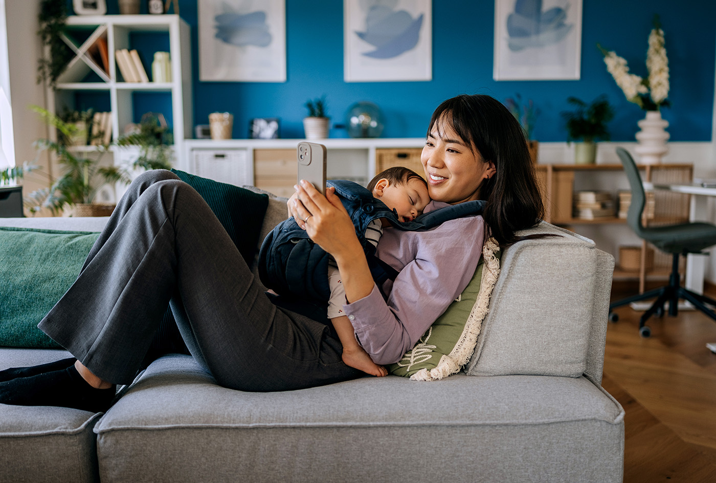 Woman looking at her phone while a baby sleeps on her chest