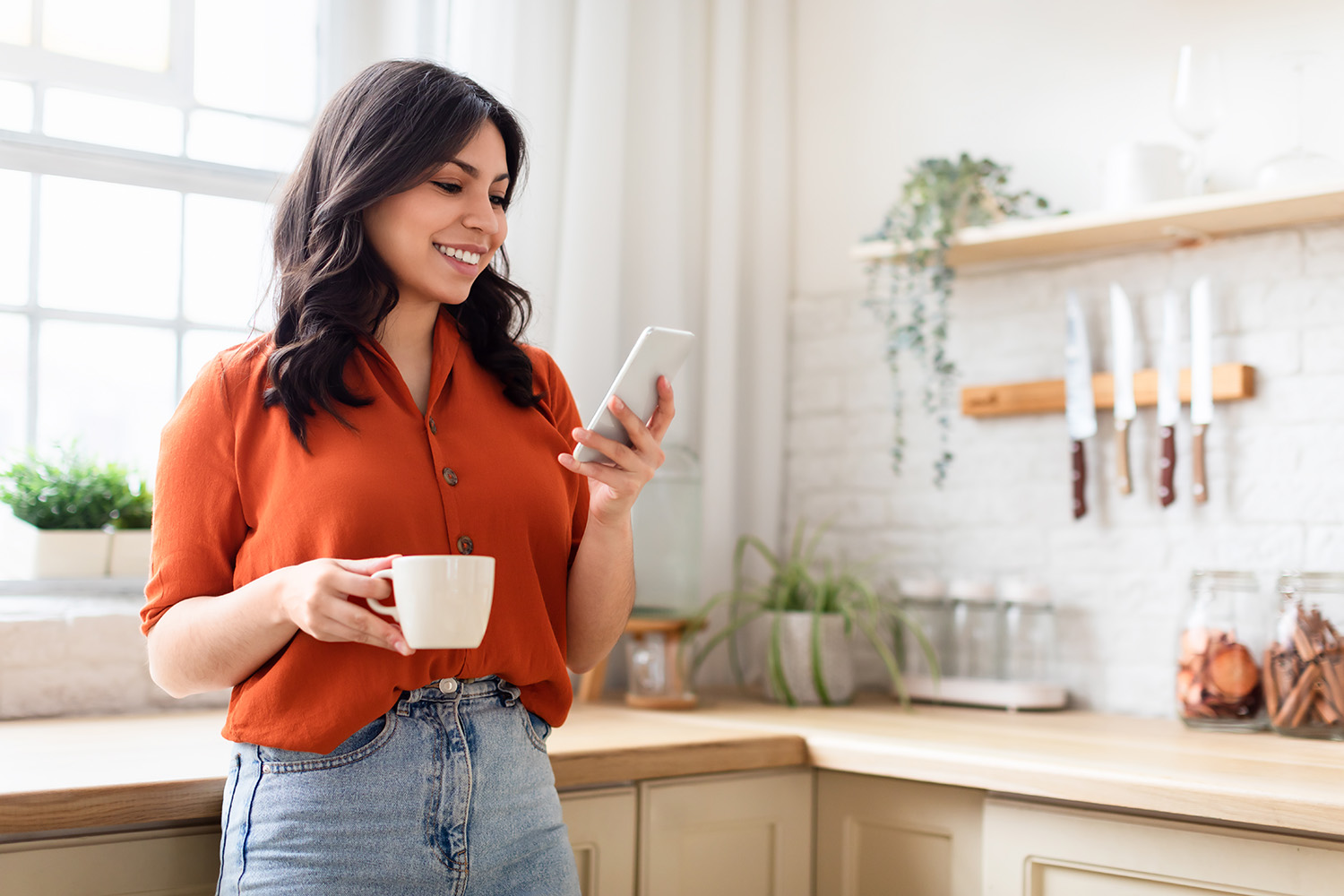 A CSAA customer standing in her kitchen with a cup of coffee, looking at the MyPolicy app on her smartphone