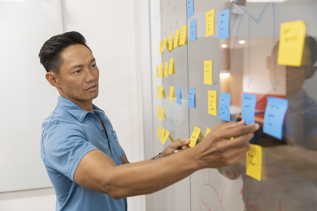 A male CSAA employee adding sticky notes to a window during a brainstorming session