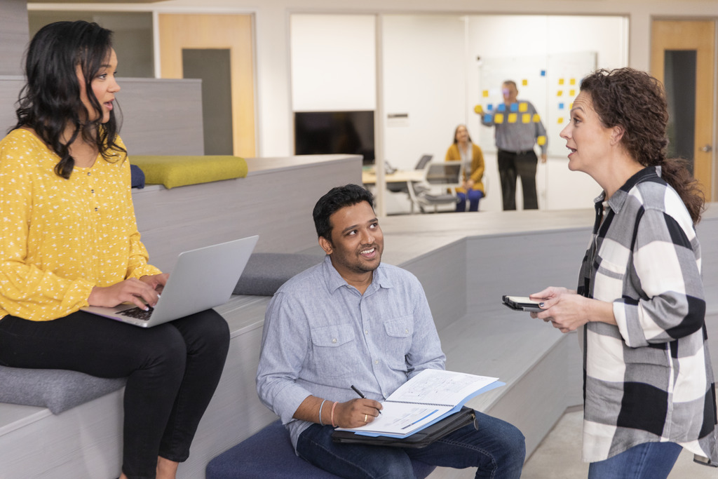 Three CSAA employees - a man and two women - interacting in an office common space