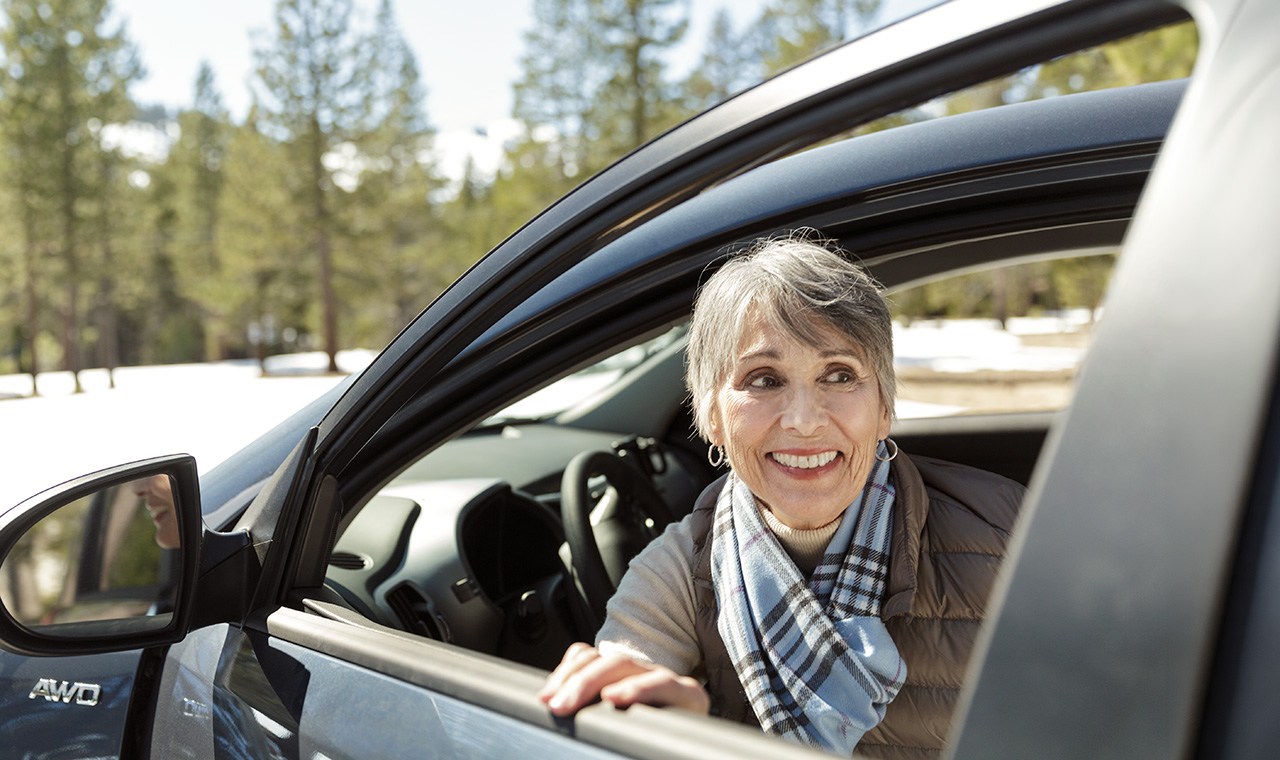A smiling senior woman looking out the driver side window of a car in the snow. senior drivers