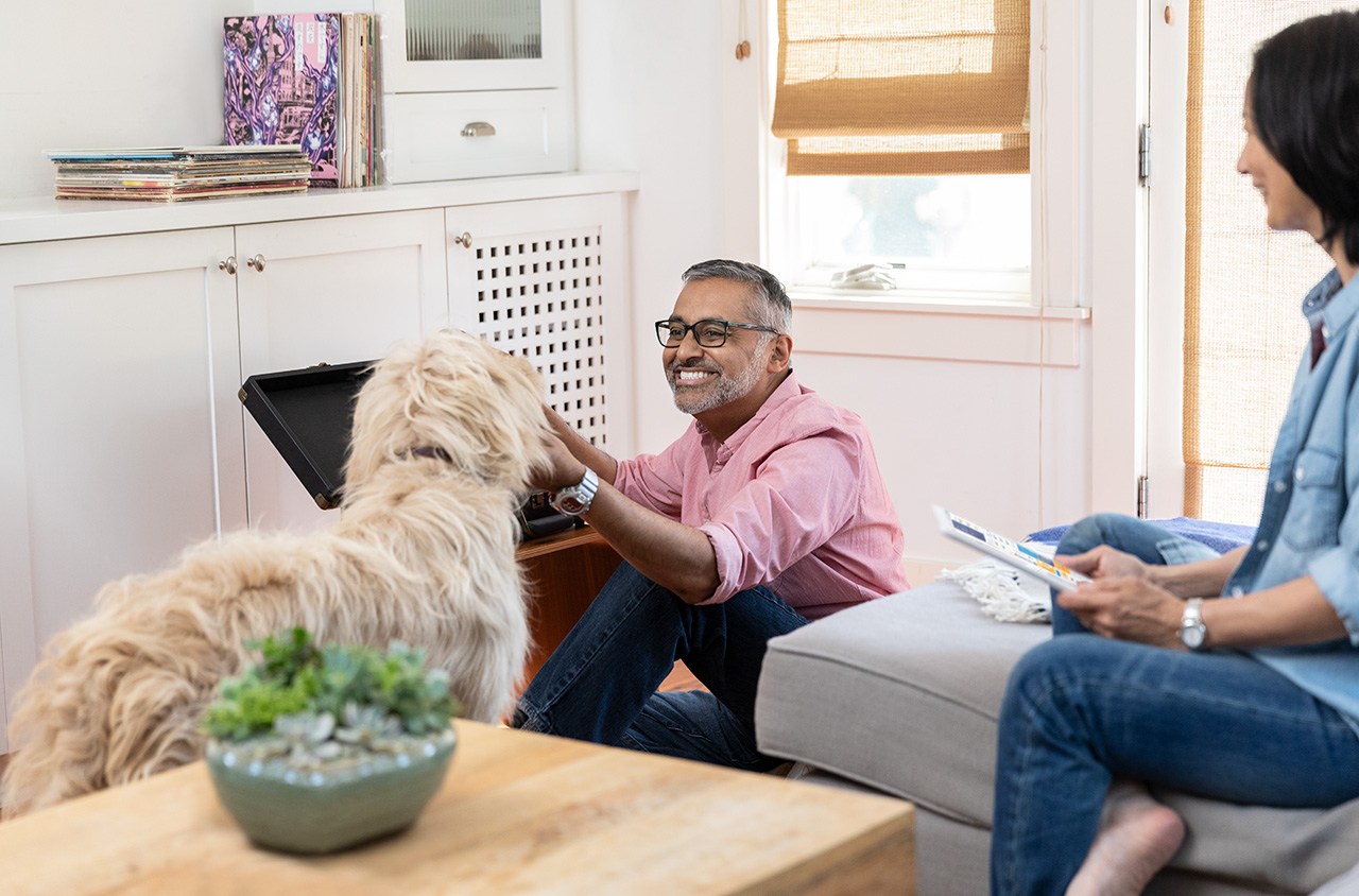 A man happily pets his dog while sitting on the floor of his living room. natural disasters