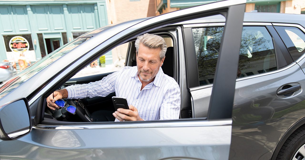 A man looks at his phone while sitting in the driver seat of a parked car. distractive driving